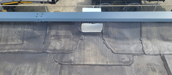 Close-up van een plat dak met reparaties aan de dakbedekking en een wit afvoerpunt