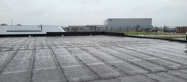 Groot plat dak met waterdichte dakbedekking en zicht op een industrieel landschap.